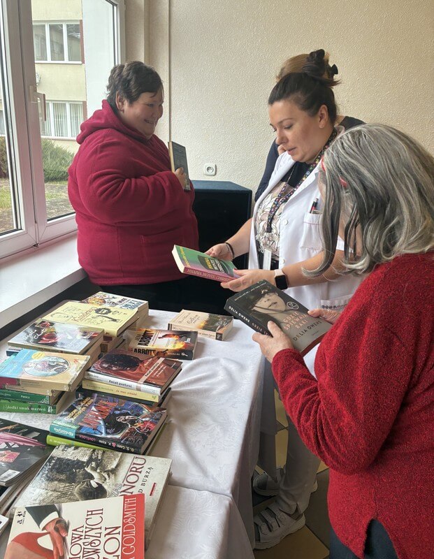 Trzy kobiety, uczestniczki spotkania, oglądają książki leżące na stole.