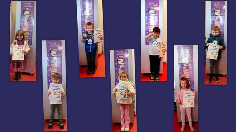 Dzieci uhonorowane dyplomami i orderami pozują do fotografii na tle miarki, promującej akcję czytelniczą Mała Książka – Wielki Człowiek. Fotografie tworzą kolaż. Tło w kolorze fioletowym.